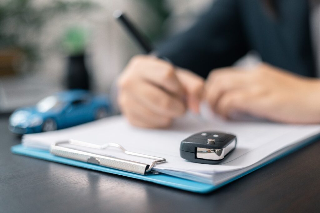 Firma del contratto di noleggio con chiavi dell’auto in primo piano.