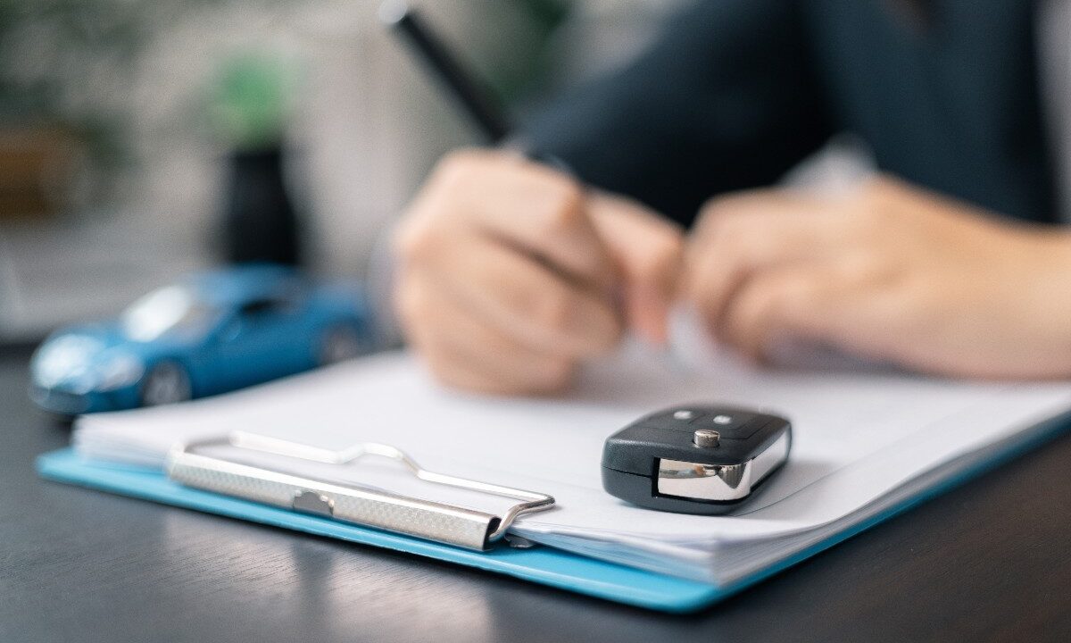 Firma del contratto di noleggio con chiavi dell’auto in primo piano.