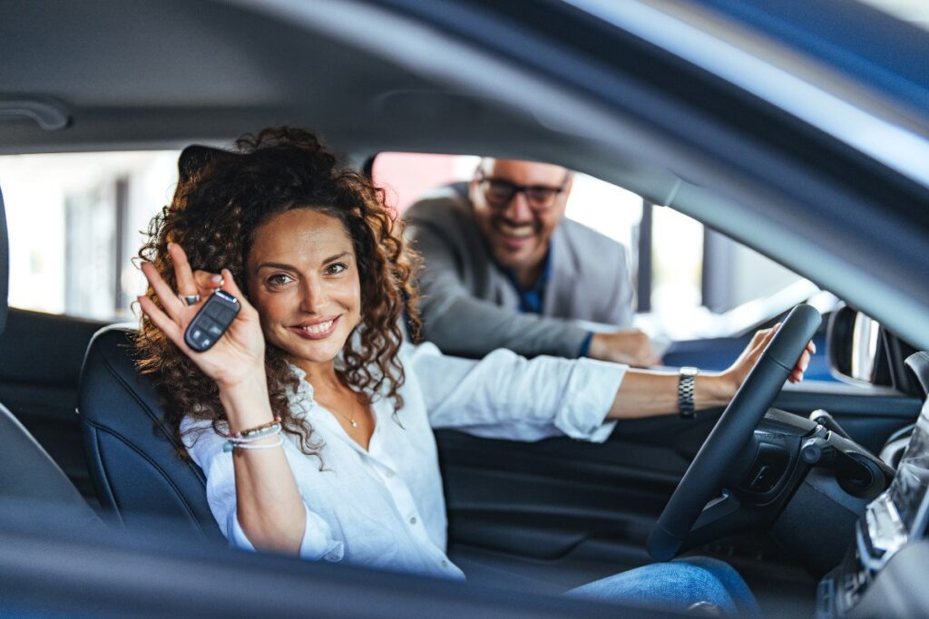 Una donna al volante mostra le chiavi della sua auto nuova.