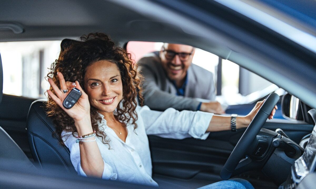 Una donna al volante mostra le chiavi della sua auto nuova.
